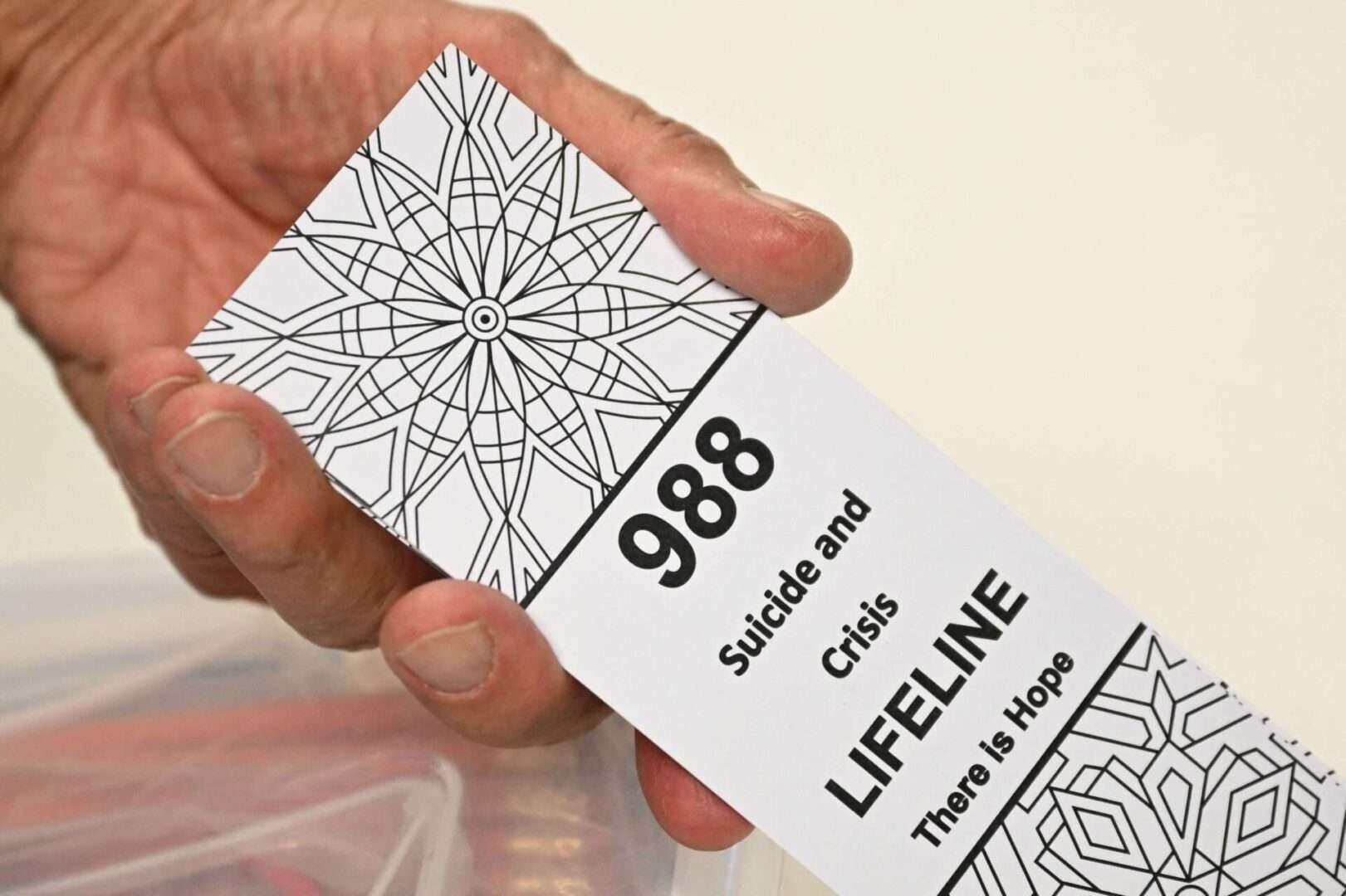 A bookmark for children with the 988 suicide and crisis lifeline emergency telephone number is displayed by Lance Neiberger, a volunteer with the Natrona County Suicide Prevention Task Force. One year after the national launch of 988, officials say the focus now is on raising awareness about the hotline. 