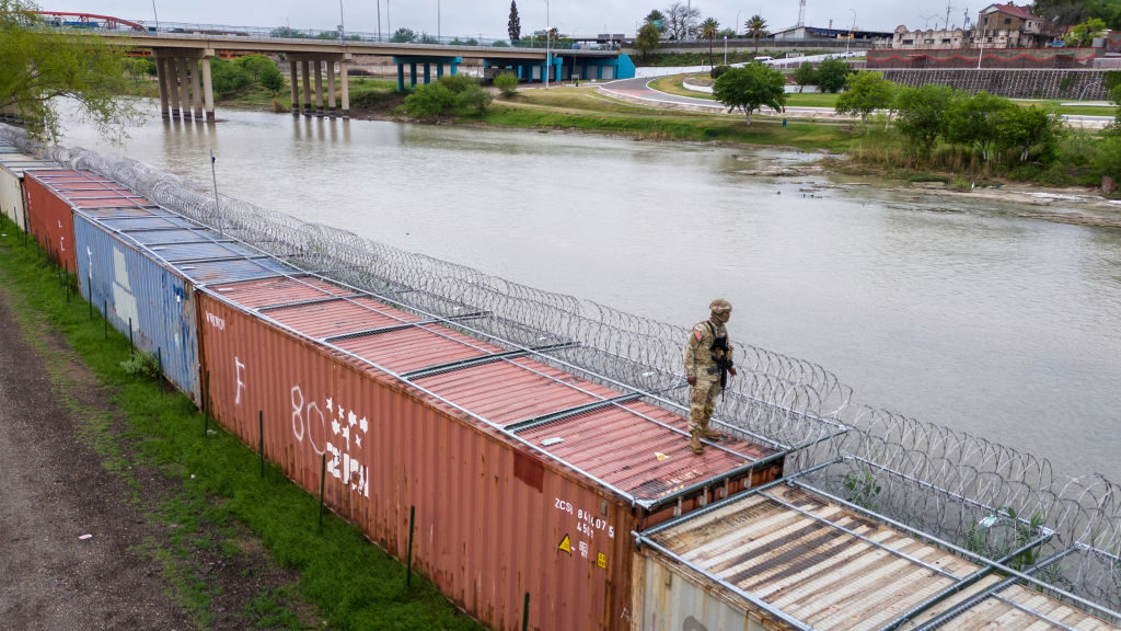 In an aerial view, a Texas National Guard soldier stands atop a barrier of shipping containers and razor wire while guarding the U.S.-Mexico border in Eagle Pass, Texas, on Sunday.